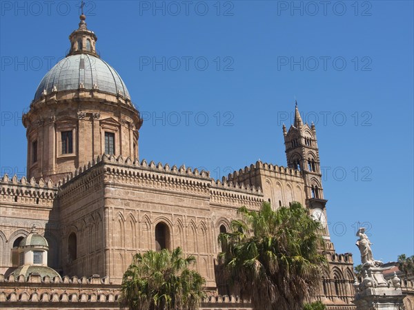 Historic cathedral with large dome and small town character, surrounded by palm trees, under a blue sky, two red towers in front of the panorama of a large city, Barcelona, Spain, Europe