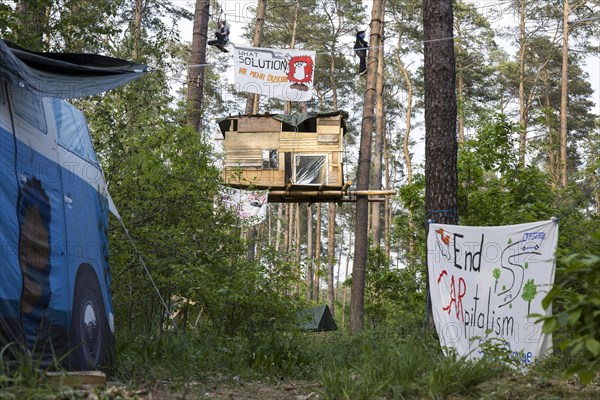 Two people swinging over a tree house in the occupied forest section Tesla Stop . In the foreground a banner End CARpitalism . The occupation of the forest is intended to demonstrate against the imminent clearing for the planned expansion of the Tesla Gigafactory in Gruenheide. 11.05.2024