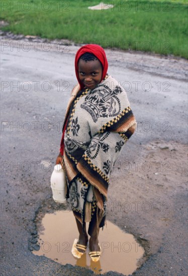 Girl washing her shoes in a puddle, rainy day in Lesotho, girl from the Basotho ethnic group, mosotho child wearing the traditional blanket