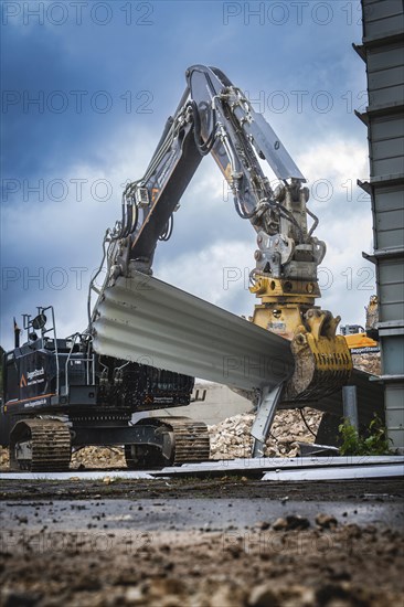 A large excavator lifts building materials on a construction site, the sky is cloudy and the surroundings look industrial, Demolition, Saarbruecken, Germany, Europe