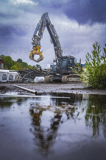 A large excavator on a construction site is reflected in a puddle under a cloudy sky, Demolition, Saarbruecken, Germany, Europe
