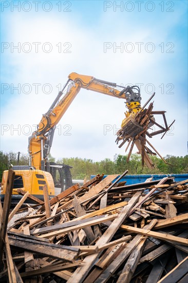 Large excavator lifts wood debris on a construction site under a cloudy sky and numerous containers, demolition, Saarbruecken, Germany, Europe