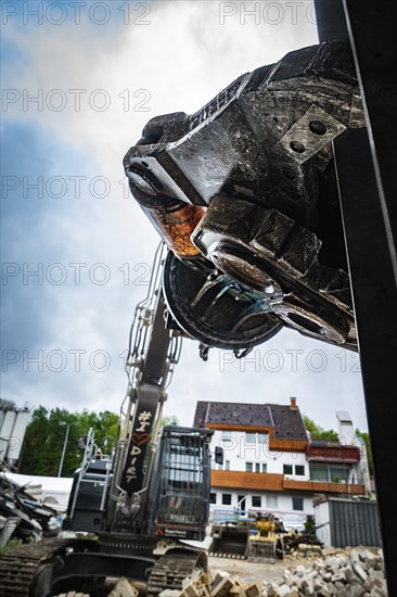 An excavator with a large claw on a demolition site, in the background several buildings and cloudy sky, demolition, Saarbruecken, Germany, Europe