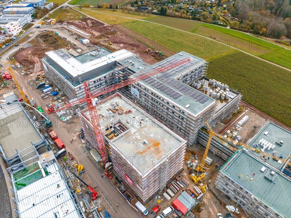 Construction site with several buildings under construction, cranes and vehicles, surrounded by green fields and rural surroundings, construction site new hospital, Calw Black Forest Germany