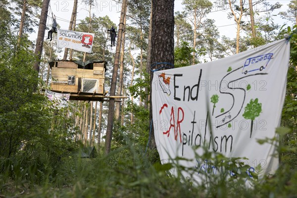 Two people swinging over a tree house in the occupied forest section Tesla Stop . In the foreground a banner End CARpitalism . The occupation of the forest is intended to demonstrate against the imminent clearing for the planned expansion of the Tesla Gigafactory in Gruenheide. 11.05.2024
