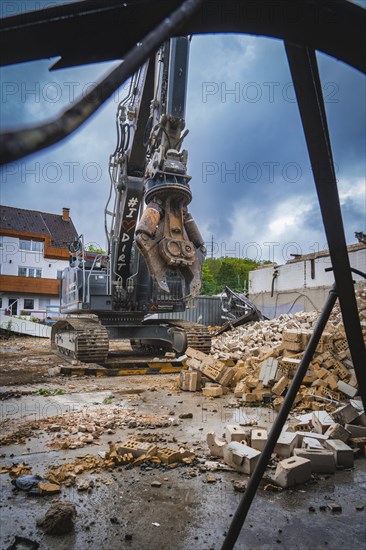 An excavator stands on a construction site, surrounded by rubble and bricks, under a cloudy sky, demolition, Saarbruecken, Germany, Europe