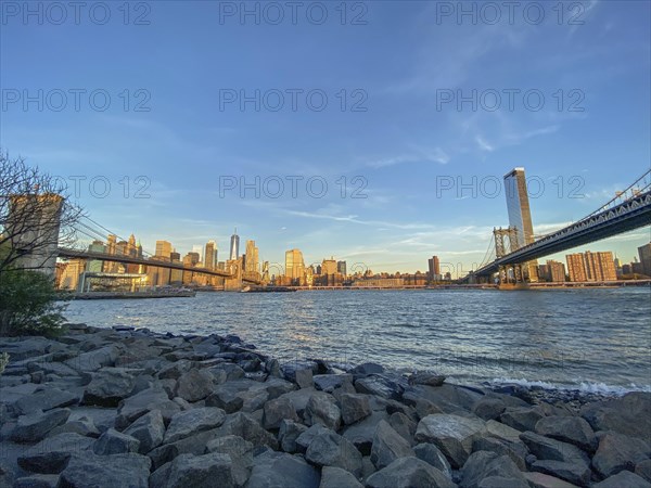 Manhattan skyline with bridges over the river at sunset seen from the shore, historic bridge in the morning light in front of the skyline of New york, new york, usa