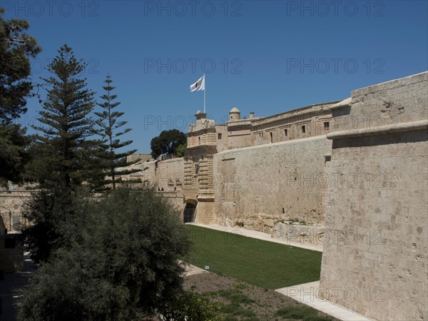 Historic fortress with protective stone walls, wide green spaces and a waving flag under a bright blue sky, the town of mdina on the island of malta with historic houses, colourful balconies, magnificent churches, mdina, Malta, Europe