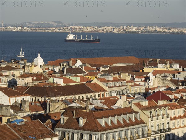 Wide angle view of a historic city with red roofs and a cargo ship in the background in the water, view of the old town of Lisbon on the river with red roofs, Lisbon, portugal