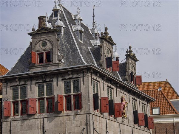 Historic building with red shutters, decorated roof and sculptures under a cloudy sky, historic houses in Hoorn and ships in the harbour, hoorn, the netherlands