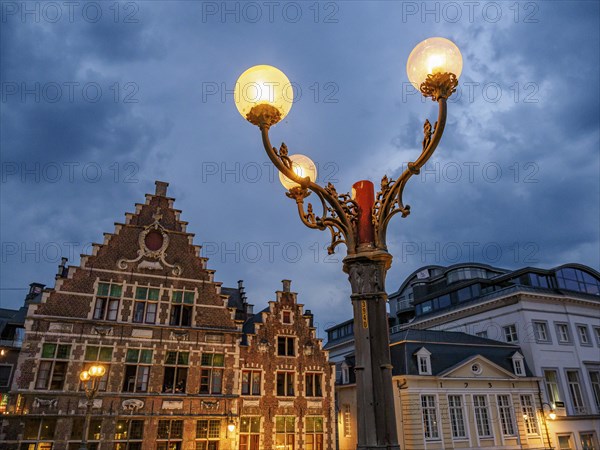 Street lamp in front of historic buildings in Bruges at night with clouds in the sky, historic buildings with towers and bridges on a river at blue hour, gent, belgium