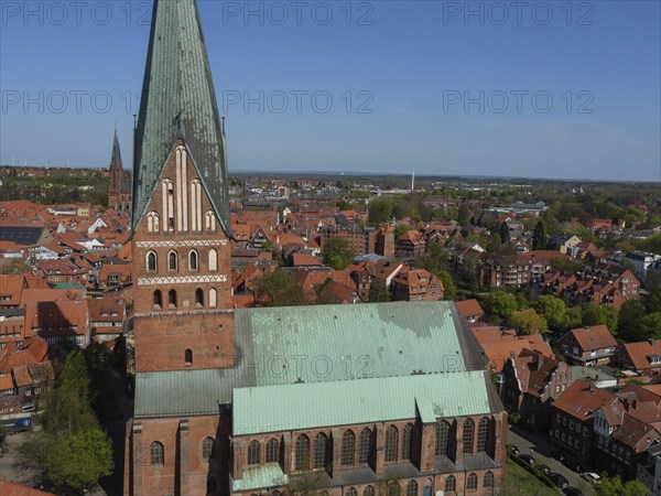 View of a gothic church with green copper roofs and a medieval cityscape under a clear sky, red brick church in North German style against a blue sky with imposing tower, Lueneburg, Germany, Europe