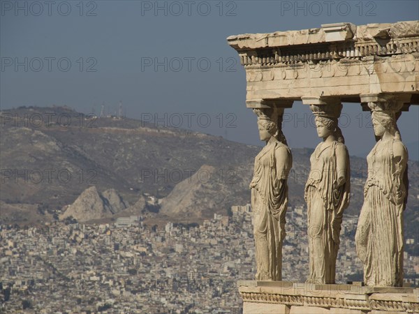 Ancient caryatid sculptures overlooking a city and mountain landscape, ancient columns against a blue sky, athens, greece