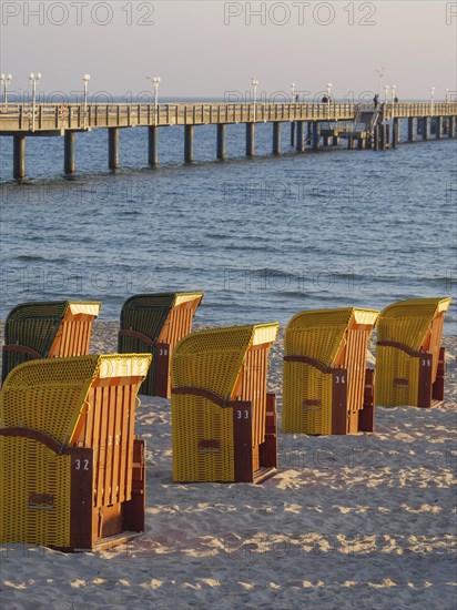 A pier stretches into the sea, surrounded by beach chairs on the sandy beach in the warm evening light, autumn atmosphere on the beach of Binz with trees beach chairs in the morning light, Binz, germany