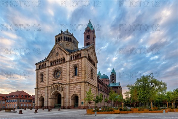 Grosse Kathedrale mit beeindruckenden Tuermen, umgeben von Baeumen im sanften Licht des Abendhimmels, die eine friedliche Atmosphaere schafft, Speyer, Rheinland Pfalz