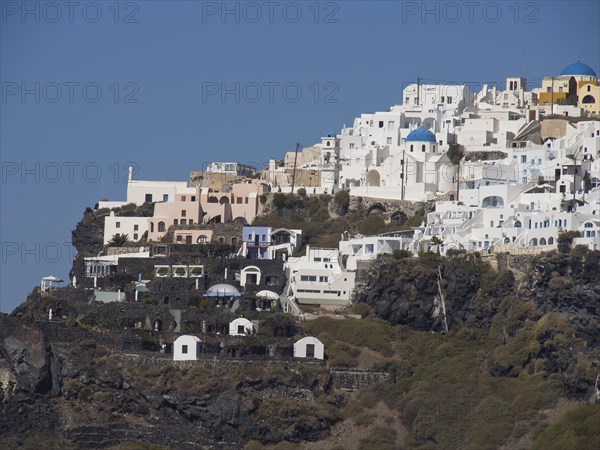 View of white buildings with blue domes on a cliff under a clear blue sky, The volcanic island of Santorini with blue and white houses and churches, flowers and palm trees on a volcanic island, santorini, greece