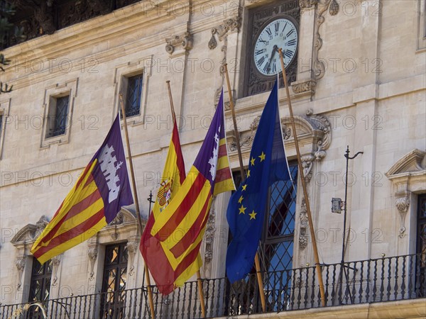 Historic building with four flags and a clock on the facade, palma de Majorca with its historic houses, the great cathedral and flowers, palma, spain
