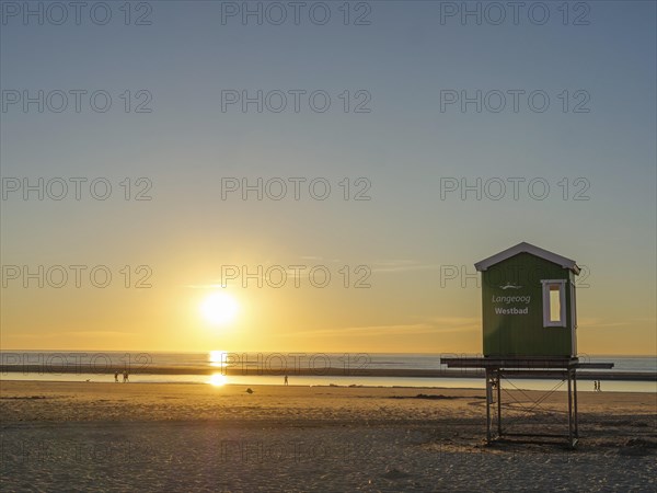 Sunset on the beach with a green wooden hut, peaceful sea and golden sky, evening mood on the beach with a sunset over the sea, beach chairs in the sunset, lnageoog, germany