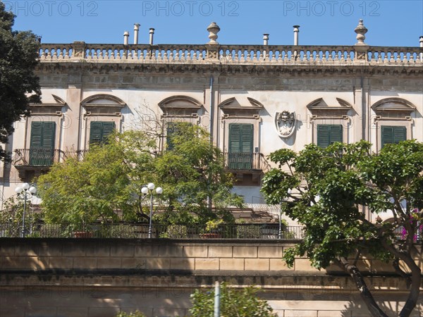 Historic building with green shutters and garden in a sunny setting, palermo in sicily with an impressive cathedral, monuments and old houses with balconies, palm trees and flowers in italy, palermo, sicily