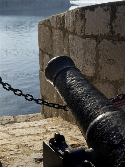 Close-up of a black cannon on an old stone wall overlooking the sea, the old town of Dubrovnik with historic houses, churches, red roofs and fortress walls, dubrovnik, coratia