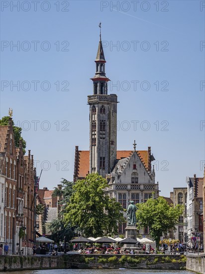 Historic building on the canal in Bruges with a cafe and blue sky on a sunny day, historic houses and churches with towers on a river in Belgium, Bruges, Belgium, Europe