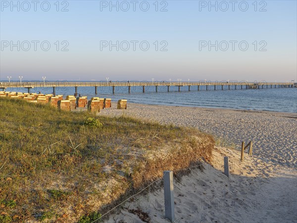 Pier leading into the calm sea, grass-covered dunes in the foreground at sunset, autumn atmosphere on the beach of Binz with trees beach chairs in the morning light, Binz, germany