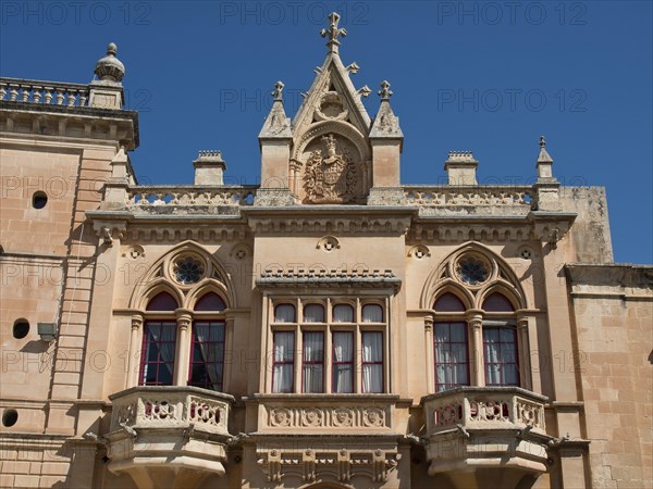 Magnificent facade with ornate windows and balconies and a magnificent coat of arms under a bright blue sky, the town of mdina on the island of malta with historic houses, colourful balconies, magnificent churches, mdina, Malta, Europe