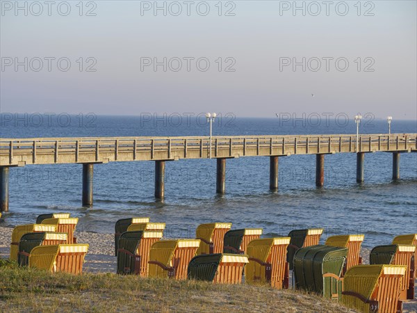 Beach chairs on the beach in front of a long pier leading into the sea, in the warm colours of the sunset, autumn atmosphere on the beach of Binz with trees beach chairs in the morning light, Binz, germany