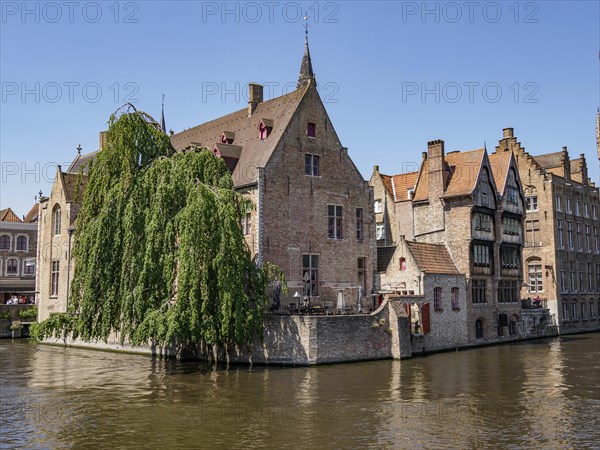 Historic building on the canal in Bruges with a cafe and blue sky on a sunny day, historic houses and churches with towers on a river in Belgium, Bruges, Belgium, Europe