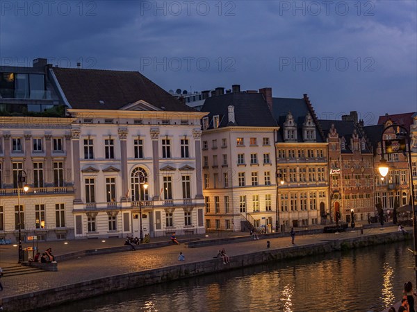 Illuminated historic buildings at dusk along the waterfront in Bruges, historic buildings with towers and bridges on a river at the blue hour, gent, belgium
