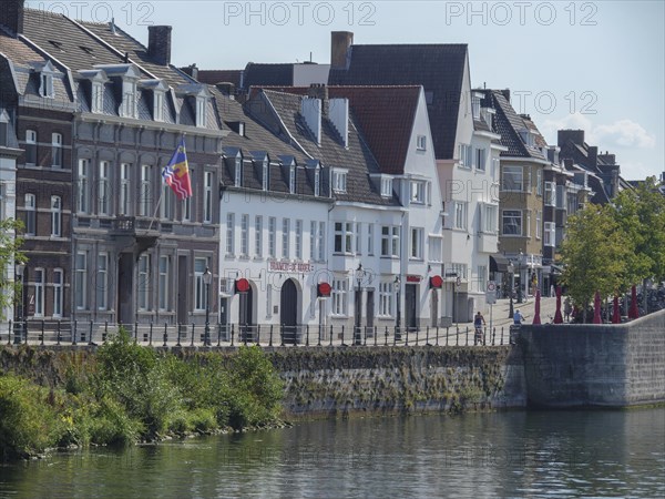 Rows of old town houses along the river under a clear sky with a visible flag, Maastricht, Netherlands