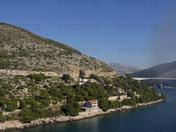Coastal landscape with mountains, hills, bridges and houses on the shore of the calm blue sea under a clear sky, the old town of Dubrovnik with historic houses, churches, red roofs and fortress walls, dubrovnik, coratia