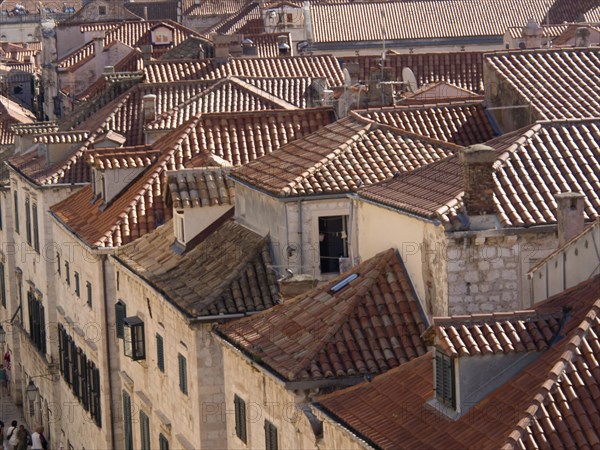 View over a collection of tiled roofs in an old town, with historic buildings and narrow streets in warm colours, the old town of Dubrovnik with historic houses, churches, red roofs and fortress walls, dubrovnik, coratia