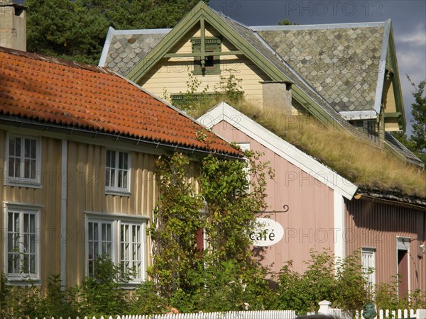 Different coloured houses with a cafe sign and green vegetation, colourful wooden houses behind white wooden fences, Molde, Norway, Europe