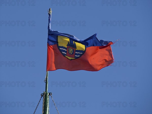 A flag with a coat of arms fluttering vividly in the wind against a clear blue sky, Borkum, Germany, Europe