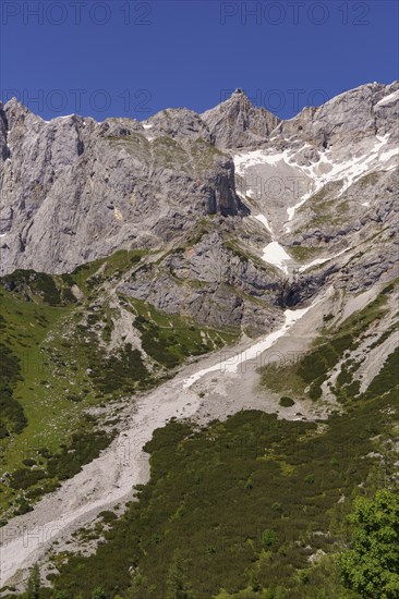 Steep alpine wall with remnants of snow and green slopes under a clear blue sky, rugged mountains with rock faces and snow-covered peaks, Gosau, Austria, Europe