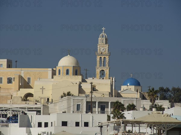 View of a church with bell tower and domes against a clear blue sky, The volcanic island of Santorini with blue and white houses and churches, flowers and palm trees on a volcanic island, santorini, greece