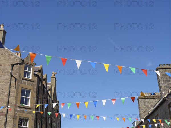 Colourful flags hang over an old town with buildings and windows under a blue sky, the atmosphere is cheerful, grey houses with colourful flags in a seaside town, lerwick, Scotland, United Kingdom, Europe