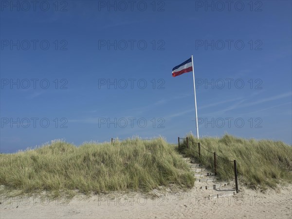 Sand dunes with stairs and flag on a sunny day under blue sky, Heligoland, Germany, Europe