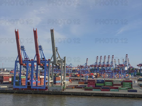 An industrial harbour terminal with lots of containers, cranes and storage areas on a sunny day, a beautiful city on the river with harbour, shipyards, houses and ships, Hamburg, Germany, Europe