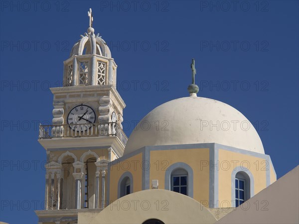 A tall bell tower and a domed church rise up against a bright blue sky, The volcanic island of Santorini with blue and white houses and churches, flowers and palm trees on a volcanic island, santorini, greece