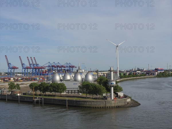 Harbour view with wind power plant, spherical tanks, containers and green trees under a clear sky, beautiful city on the river with harbour, shipyards, houses and ships, Hamburg, Germany, Europe