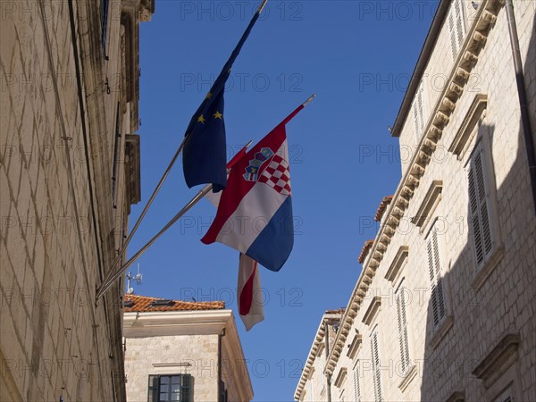 Flags of the European Union and Croatia fly in a narrow alley between historic buildings, the old town of Dubrovnik with historic houses, churches, red roofs and fortress walls, dubrovnik, coratia
