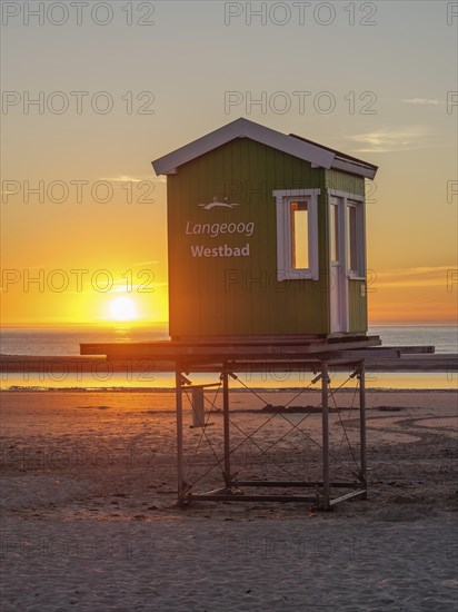 Beach hut at sunset, warm light bathes the scene in a cosy orange, setting sun on the North Sea beach with warm light over colourful beach chairs, langeoog, germany