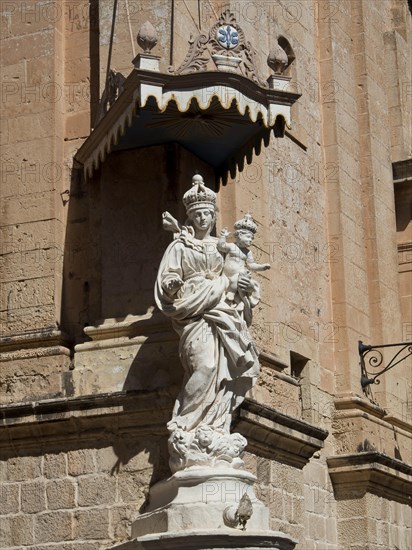 Close-up of a baroque statue on a stone house wall under a blue sky, Historic buildings with beautiful windows, balconies and small towers, Mdina, Malta, Europe