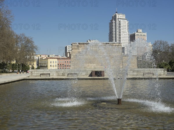 Fountain with water jets in front of historic buildings in a park under a blue sky, Madrid, Spain, Europe