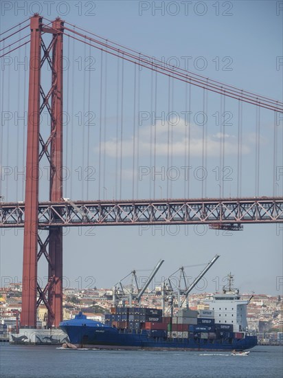 Red suspension bridge over the water, below container harbour with large cargo ships, Lisbon, Portugal, Europe