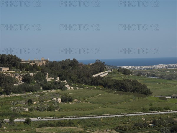 Vast green landscape with hills, trees and a city on the horizon under a clear sky, the town of mdina on the island of malta with historic houses, colourful balconies, magnificent churches, mdina, Malta, Europe