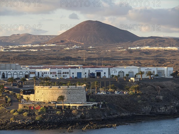 A castle and modern buildings on the coast, mountains and a volcano in the background, Lanzarote, Spain, Europe