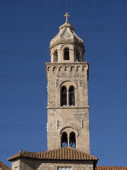 High stone church tower with a cross at the top, in front of a bright blue sky, the old town of Dubrovnik with historic houses, churches, red roofs and fortress walls, dubrovnik, coratia